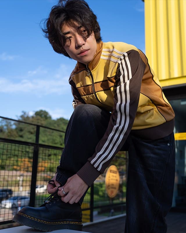 Young man in a yellow track jacket tying his boot in front of a yellow container building
