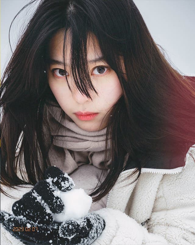 Portrait of a woman in a fleece jacket holding snow in black gloves, hair blown across her face