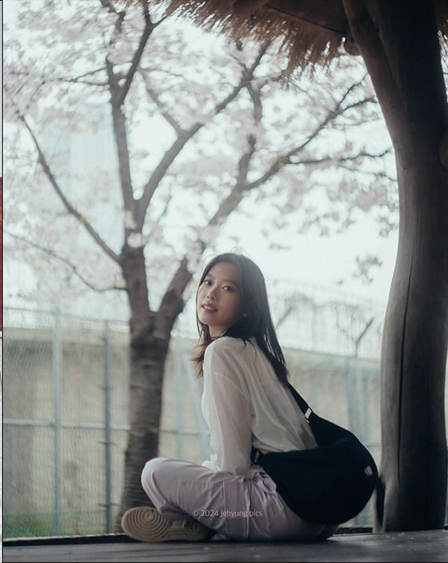 Woman sitting under a cherry blossom tree, looking back over her shoulder